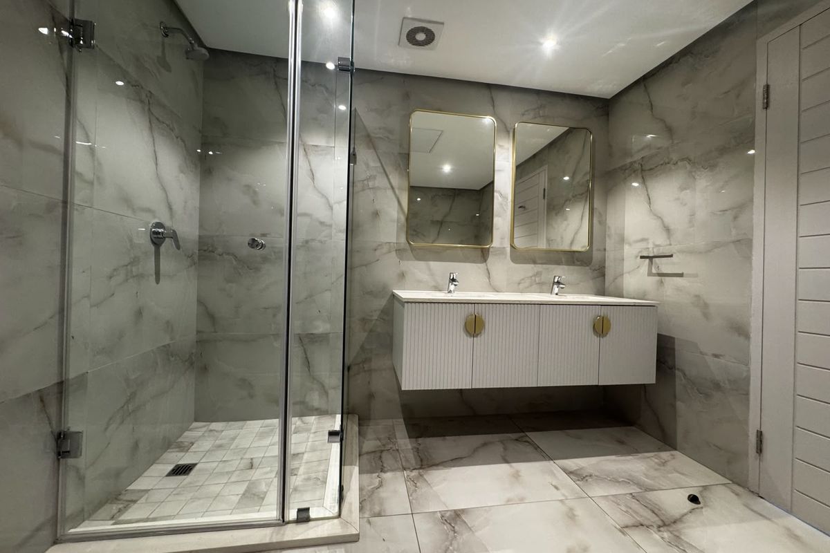 Modern bathroom featuring a double vanity with wall-mounted cabinetry, a spacious walk-in shower with glass enclosure, and elegant marble-look floor and wall tiling.
