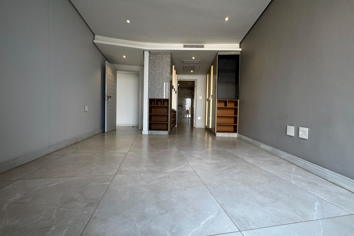 A spacious, empty bedroom featuring modern large-format floor tiles, built-in cabinetry with integrated lighting, and recessed ceiling lights.