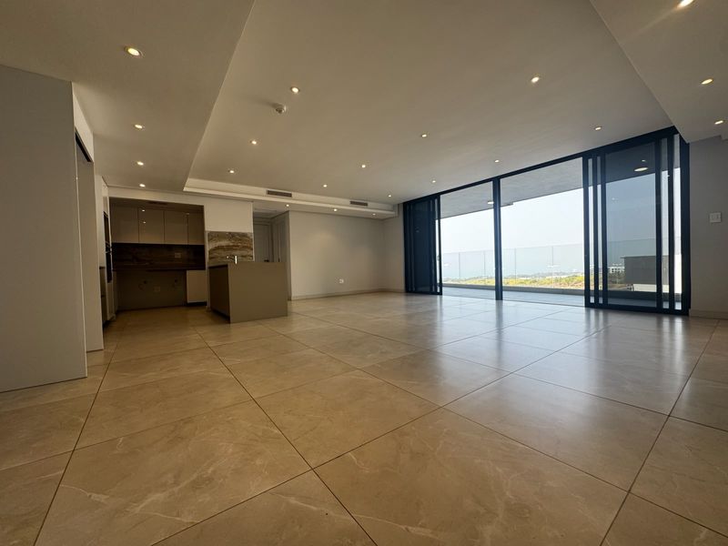 Spacious open-plan living area featuring large format floor tiles, recessed lighting, and seamless flow to a balcony with glass balustrades and expansive views.