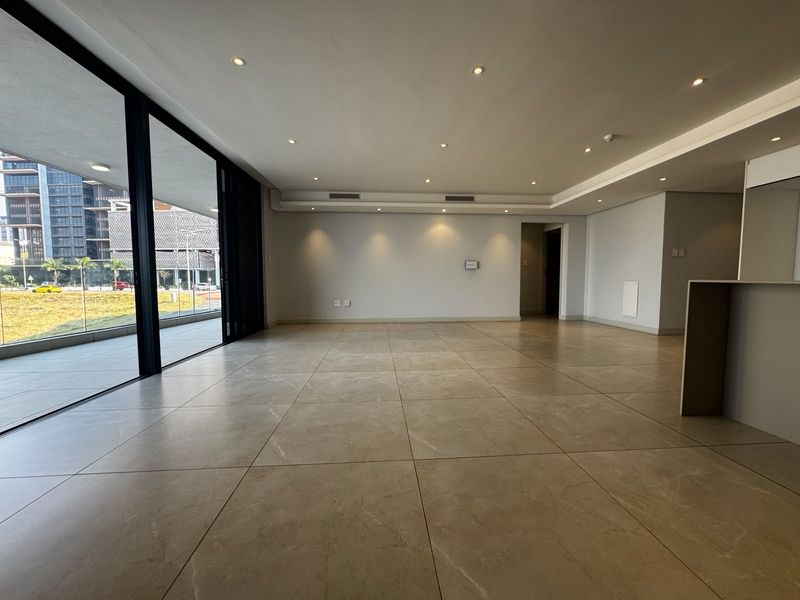 Spacious open-plan living area featuring large format floor tiles, recessed lighting, and floor-to-ceiling sliding glass doors leading to an outdoor balcony.