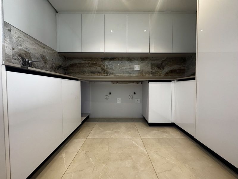 A modern, minimalist kitchen featuring glossy white cabinetry, stone-look backsplash, and tiled flooring, currently awaiting appliance installation.