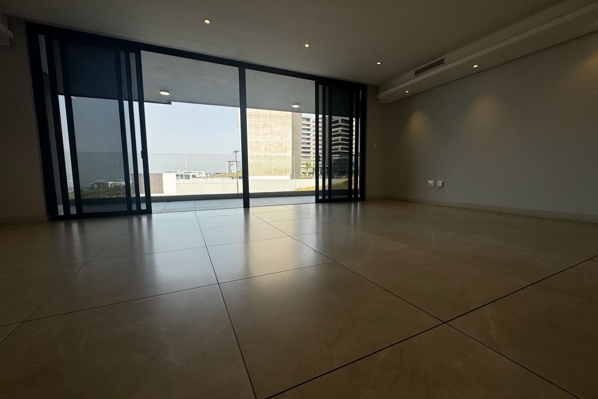 Spacious, modern open-plan living area featuring large format floor tiles, recessed lighting, and expansive sliding glass doors leading to a private balcony.