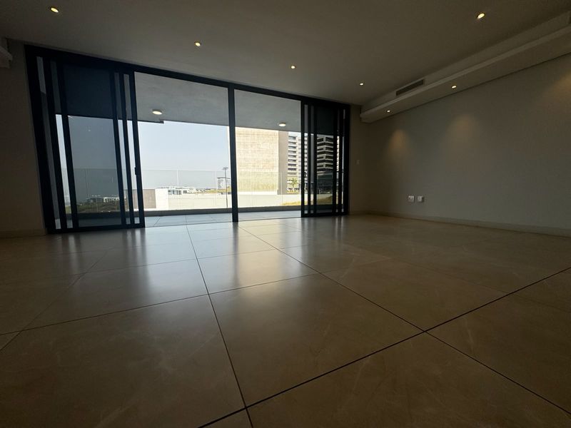 Spacious, modern open-plan living area featuring large format floor tiles, recessed lighting, and expansive sliding glass doors leading to a private balcony.