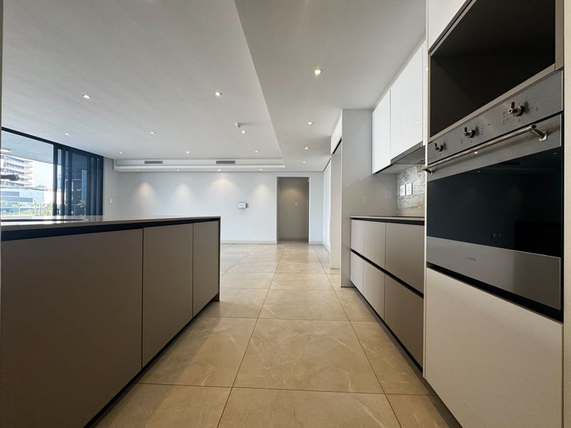 Modern open-plan kitchen and living area featuring sleek cabinetry, built-in appliances, recessed lighting, and large sliding glass doors leading to an outdoor space.