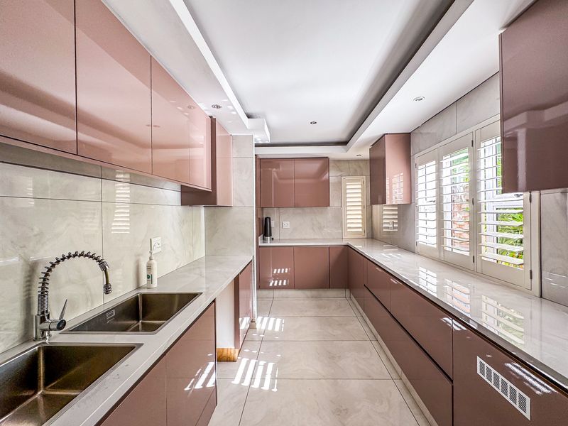 Modern kitchen featuring high-gloss cabinetry, stone countertops, double stainless steel sink, and plantation shutters, offering a clean and contemporary aesthetic.