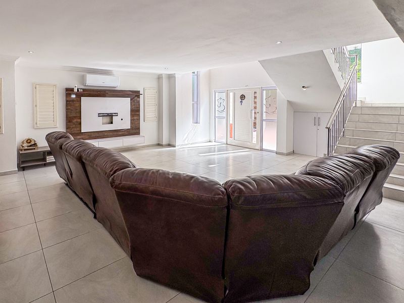 Spacious open-plan living area featuring large format floor tiles, a modern built-in media wall, and a staircase with a sleek metal balustrade.