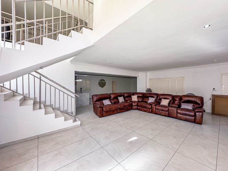 Spacious open-plan living area featuring large format floor tiles, a prominent staircase with stainless steel balustrades, and plantation shutters.