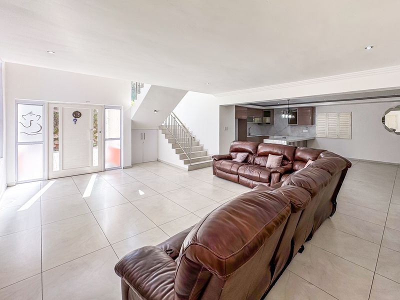 Spacious open-plan living area featuring large format floor tiles, a modern staircase with metal railing, and an integrated kitchen with island cabinetry.