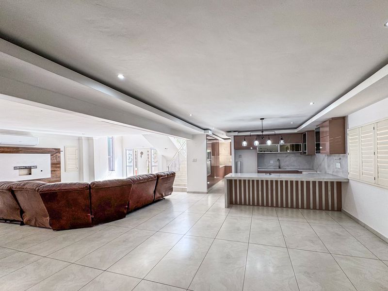 Spacious open-plan living and kitchen area featuring modern cabinetry, a central island, tiled flooring, and recessed lighting, creating a bright and functional living space.