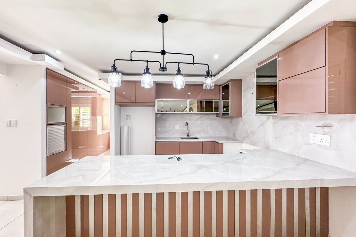 Modern kitchen featuring sleek pink cabinetry, marble-look countertops and backsplash, and a central breakfast bar with contemporary pendant lighting.