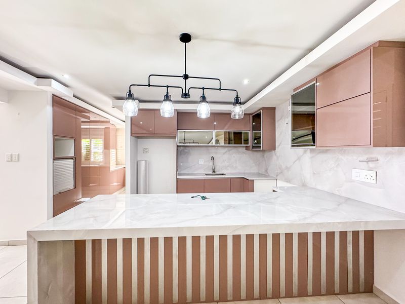 Modern kitchen featuring sleek pink cabinetry, marble-look countertops and backsplash, and a central breakfast bar with contemporary pendant lighting.
