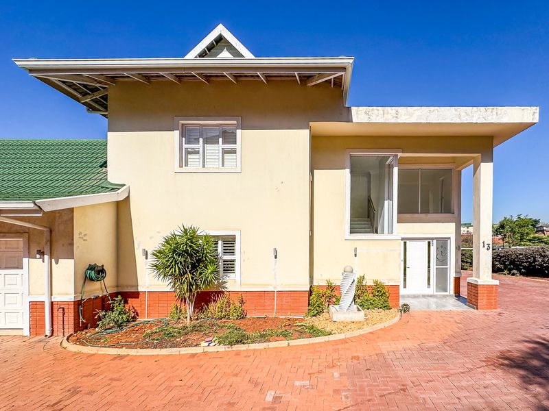 Front elevation of a townhouse featuring a brick paved driveway, covered entrance, and a combination of tiled and flat roof sections.