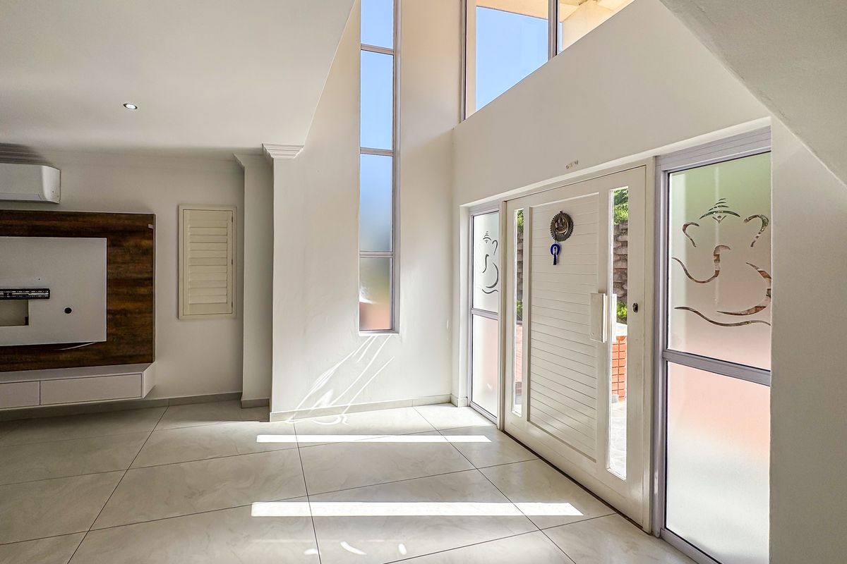 Spacious, light-filled living area featuring double volume ceilings, large windows, tiled flooring, and a modern built-in media console.