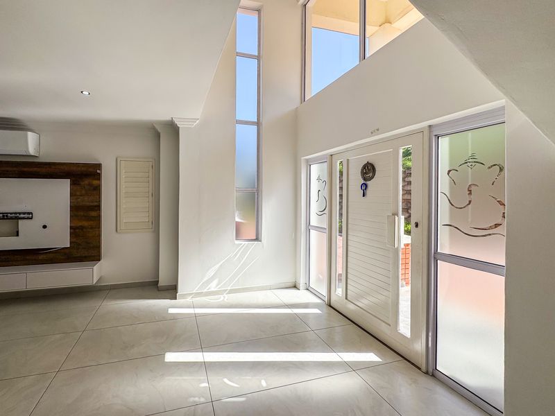 Spacious, light-filled living area featuring double volume ceilings, large windows, tiled flooring, and a modern built-in media console.