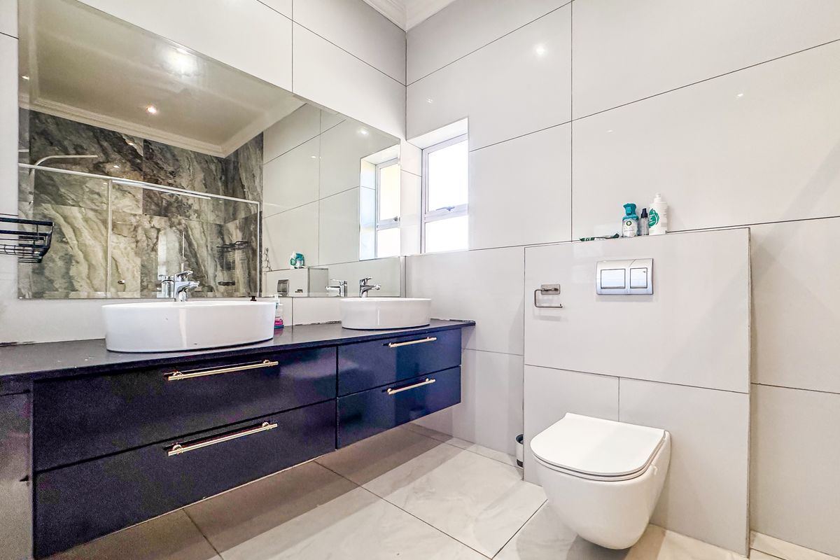 Modern bathroom featuring a sleek double vanity, wall-mounted toilet with concealed cistern, large mirror, and contemporary floor-to-ceiling tiling.