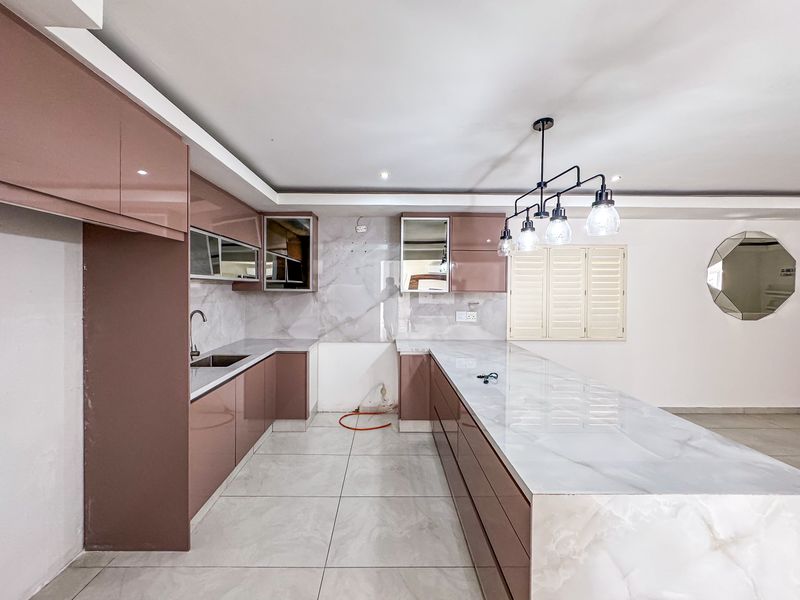 Modern kitchen featuring glossy cabinetry, a large stone-topped island, and tiled flooring, currently awaiting final finishes and appliance installation.