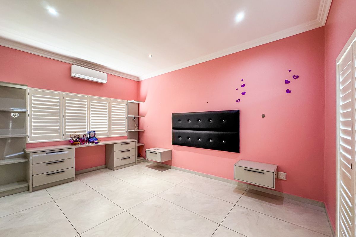 Spacious bedroom featuring tiled flooring, built-in desk and cabinetry, plantation shutters, and a wall-mounted headboard with integrated floating bedside units.