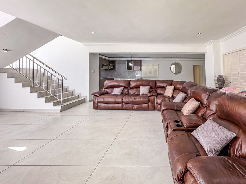 Spacious open-plan living area featuring large format floor tiles, a modern staircase with stainless steel railings, and a view into the kitchen area.