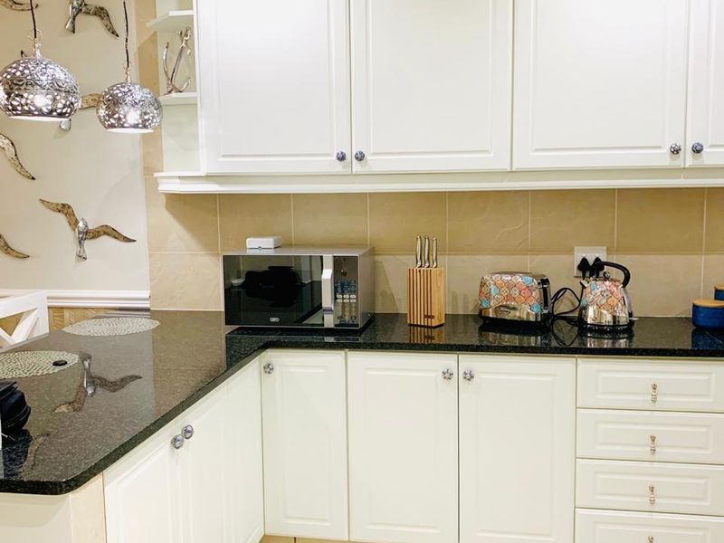 A well-maintained kitchen featuring white cabinetry, dark granite countertops, a neutral tiled backsplash, and modern pendant lighting.
