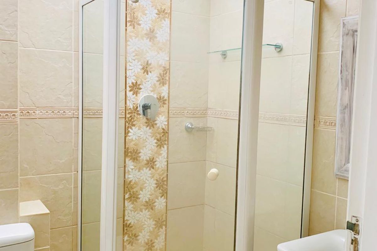 A well-maintained bathroom featuring a corner shower enclosure with decorative tile inlay, a vessel sink on a granite vanity, and a bright skylight.