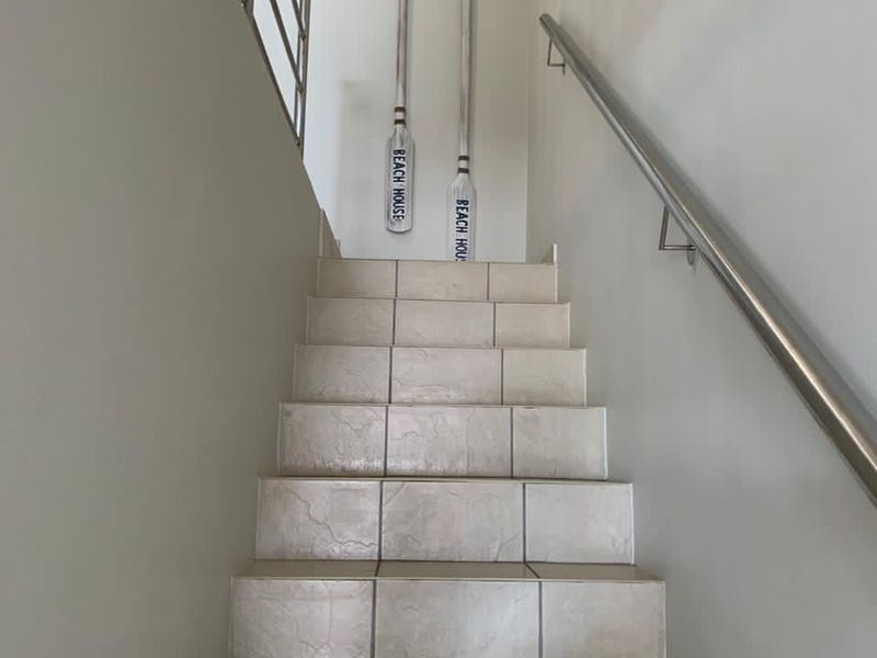 A bright staircase featuring neutral floor tiles, a modern stainless steel handrail, and a decorative glass block window providing natural light.