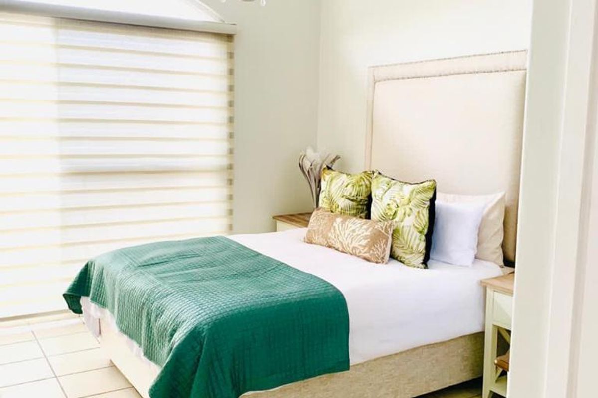A bright and airy bedroom featuring tiled flooring, exposed ceiling beams, and a large arched window with roller blinds.