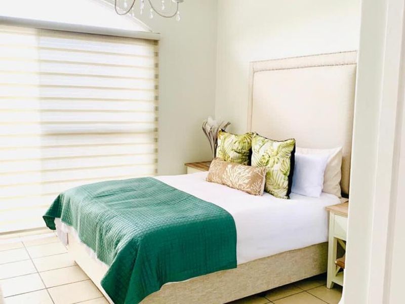 A bright and airy bedroom featuring tiled flooring, exposed ceiling beams, and a large arched window with roller blinds.
