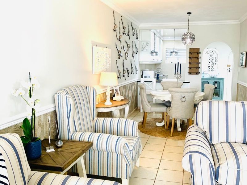 An open-plan living and dining area featuring ceramic floor tiles, decorative chair rail molding, and an arched transition leading into the kitchen space.