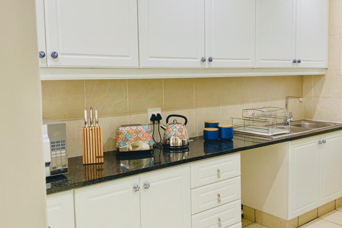 A functional kitchen featuring white shaker-style cabinetry, dark granite countertops, a tiled backsplash, and ceramic floor tiles.