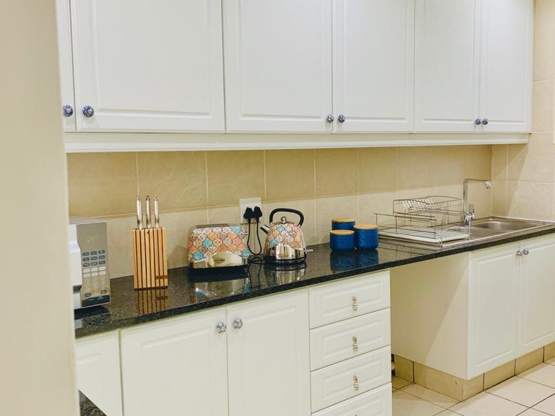 A functional kitchen featuring white shaker-style cabinetry, dark granite countertops, a tiled backsplash, and ceramic floor tiles.