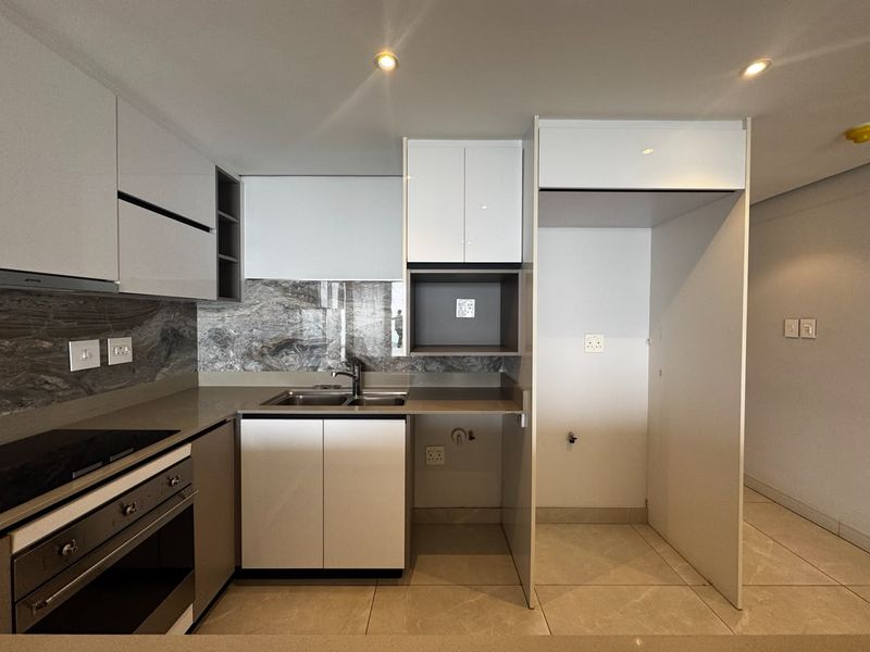 Modern kitchen featuring sleek white cabinetry, stone countertops, marble-look splashback, built-in oven, electric hob, and dedicated space for a refrigerator.