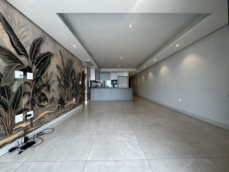 Spacious open-plan living and kitchen area featuring modern tiled flooring, recessed ceiling lighting, and a striking feature wall.