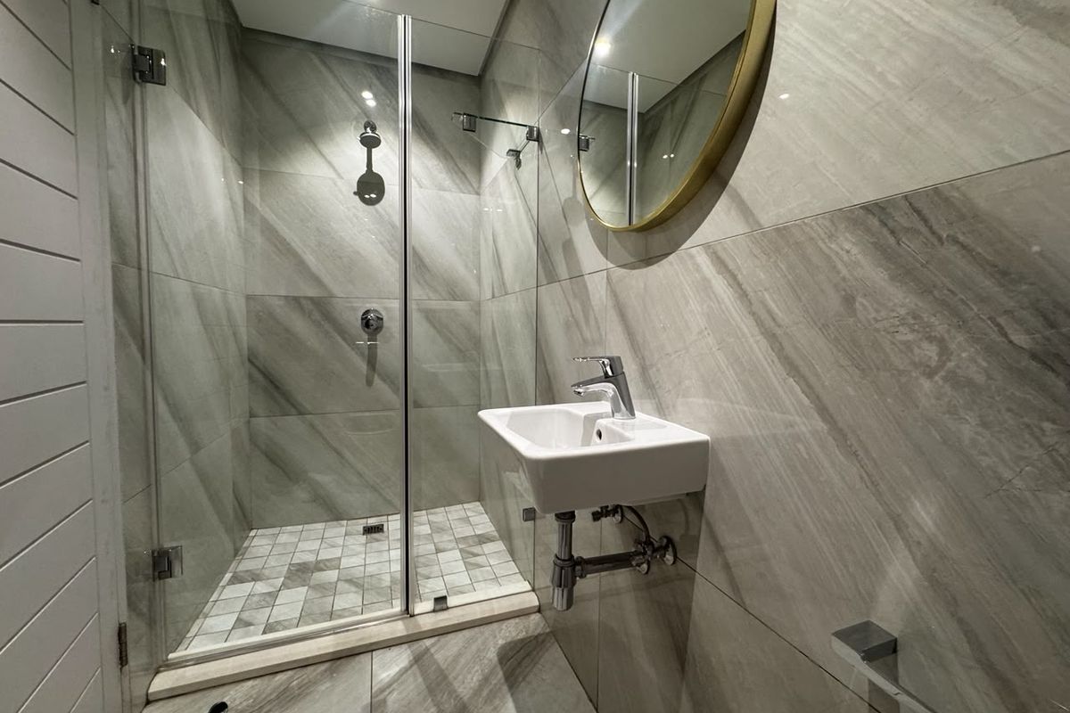 Modern bathroom featuring a walk-in shower with glass screen, wall-mounted basin, and contemporary grey porcelain tiling throughout.