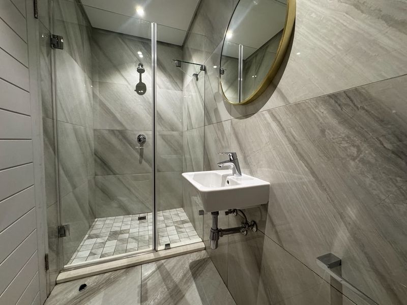 Modern bathroom featuring a walk-in shower with glass screen, wall-mounted basin, and contemporary grey porcelain tiling throughout.