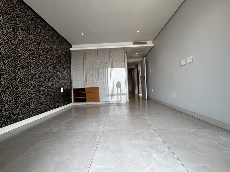A spacious, empty bedroom featuring large-format porcelain floor tiles, built-in high-gloss cupboards, and modern recessed downlighting.