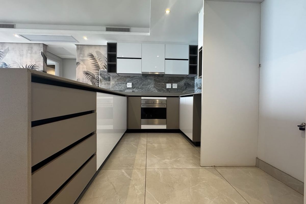Modern kitchen featuring sleek gloss cabinetry, stone countertops, built-in oven, extractor fan, and large format floor tiles in a contemporary open-plan layout.