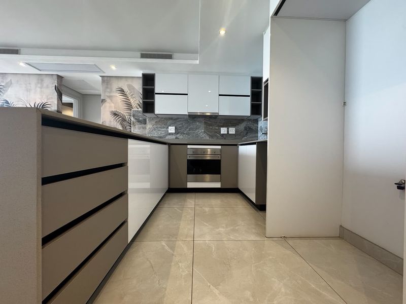 Modern kitchen featuring sleek gloss cabinetry, stone countertops, built-in oven, extractor fan, and large format floor tiles in a contemporary open-plan layout.