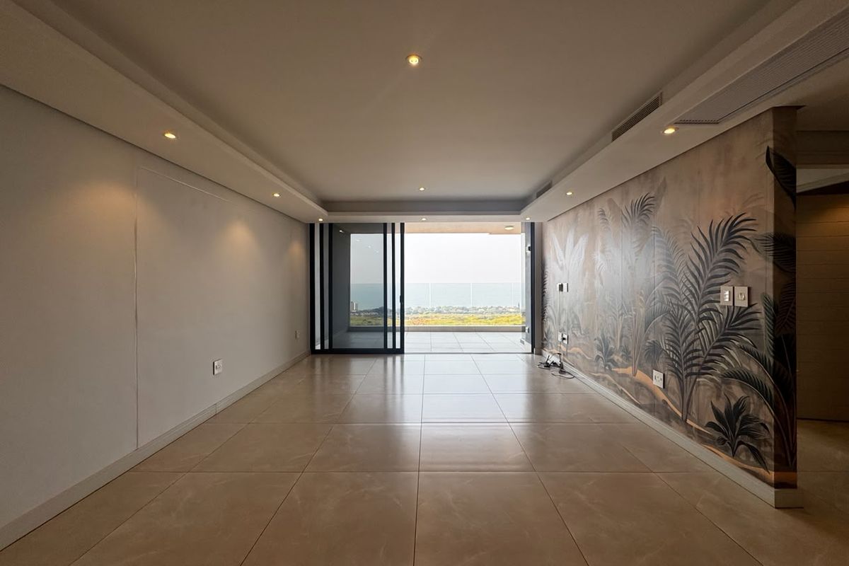 Spacious, empty living area featuring large format floor tiles, recessed lighting, and a decorative feature wall, opening onto a balcony with scenic views.
