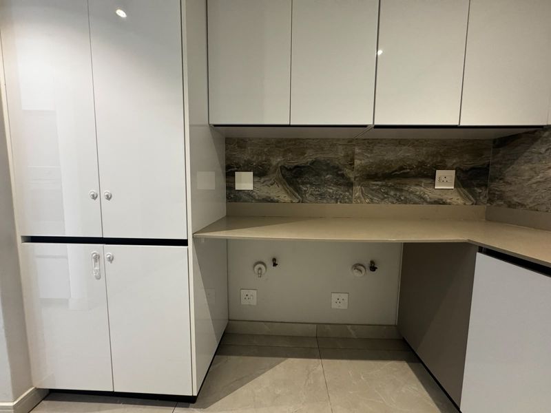 A modern, clean laundry area featuring sleek white built-in cabinetry, stone countertops, and a decorative stone splashback with dedicated plumbing and electrical connections.