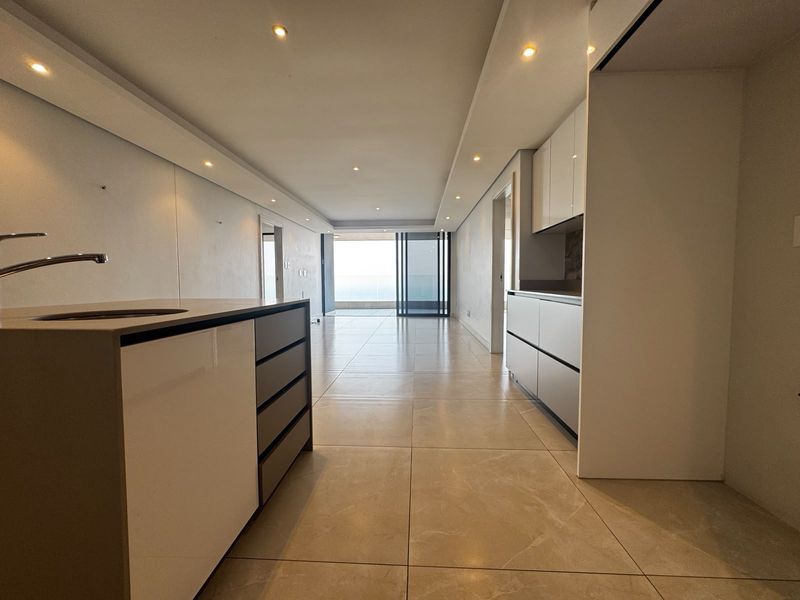 Modern open-plan living and kitchen area featuring sleek cabinetry, tiled floors, recessed lighting, and seamless access to an outdoor balcony.