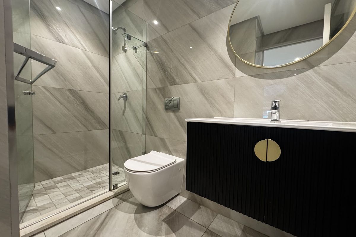 Modern bathroom featuring large-format grey stone-look tiles, a walk-in glass shower, wall-hung toilet with concealed cistern, and a contemporary black vanity unit.