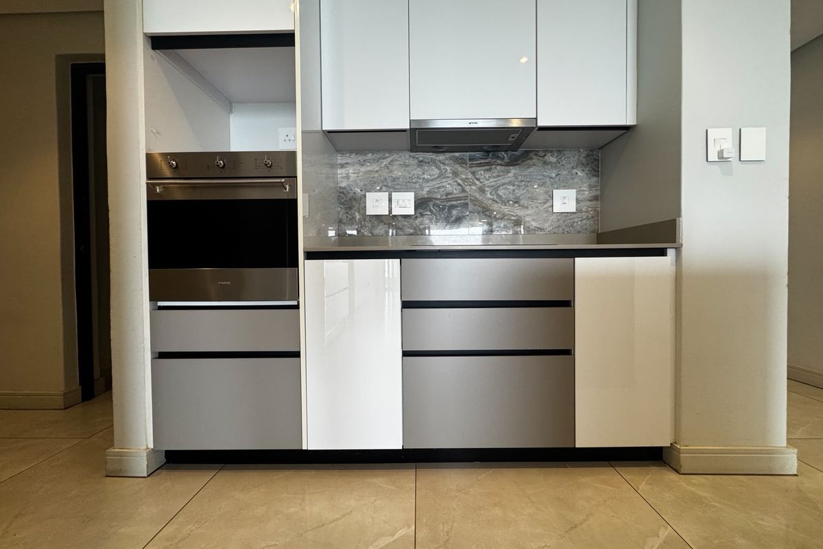 Modern kitchen featuring high-gloss cabinetry, built-in oven, extractor fan, and stone splashback with neutral tiled flooring.
