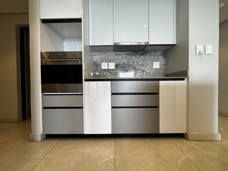 Modern kitchen featuring high-gloss cabinetry, built-in oven, extractor fan, and stone splashback with neutral tiled flooring.