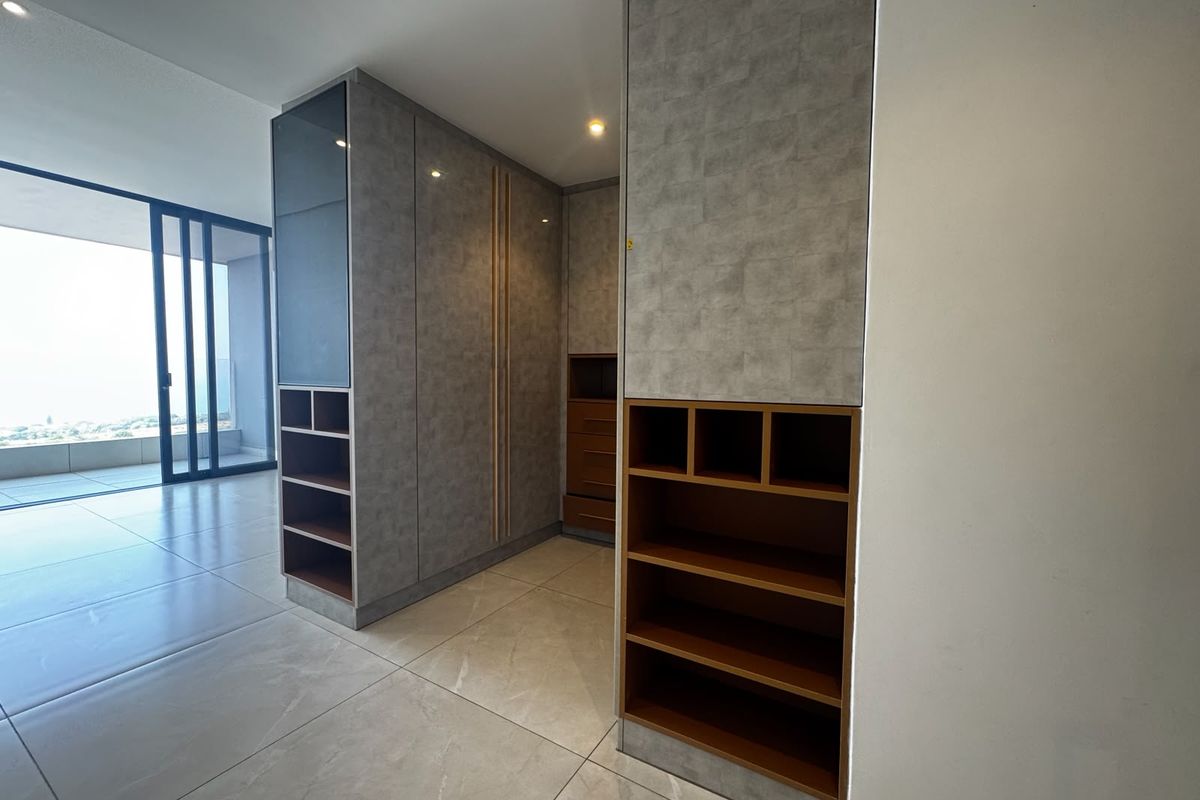 Modern bedroom featuring extensive built-in cabinetry with integrated shelving and large sliding glass doors leading to an outdoor balcony area.