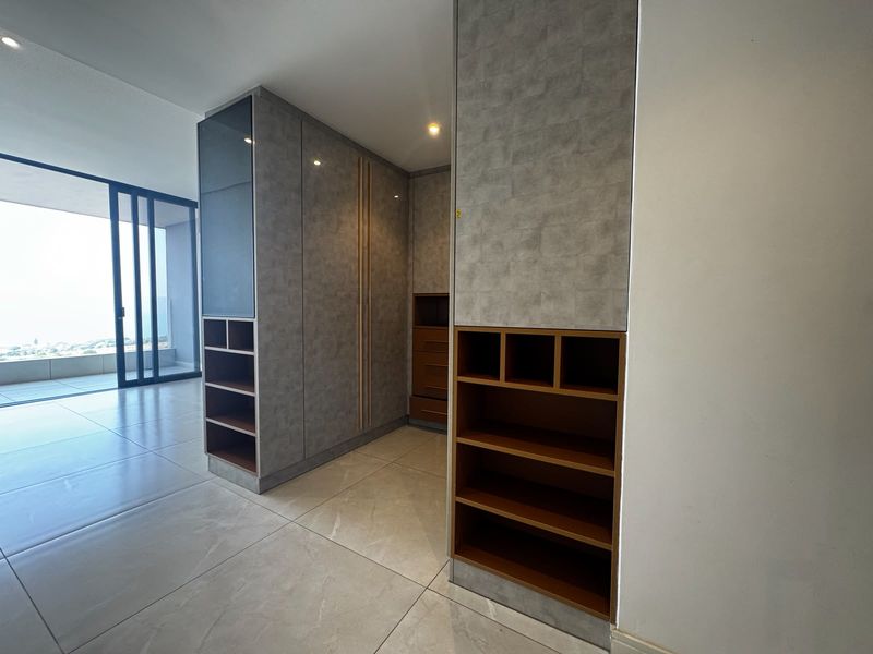 Modern bedroom featuring extensive built-in cabinetry with integrated shelving and large sliding glass doors leading to an outdoor balcony area.