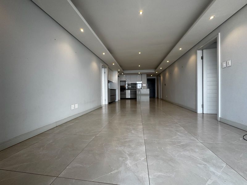 Spacious open-plan living area featuring modern tiled flooring, recessed ceiling lighting, and a sleek, contemporary kitchen with built-in cabinetry.