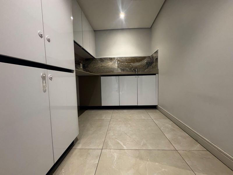 A modern, clean scullery featuring high-gloss white cabinetry, stone splashback, undermount sink, and large format tiled flooring.
