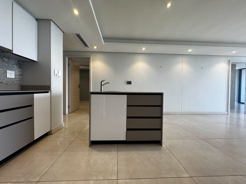 Modern kitchen featuring a central island with a mixer tap, sleek built-in cabinetry, recessed lighting, and neutral tiled flooring in an open-plan layout.
