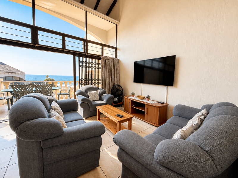 Spacious living room featuring high vaulted ceilings, large windows with ocean views, and direct access to a private balcony.