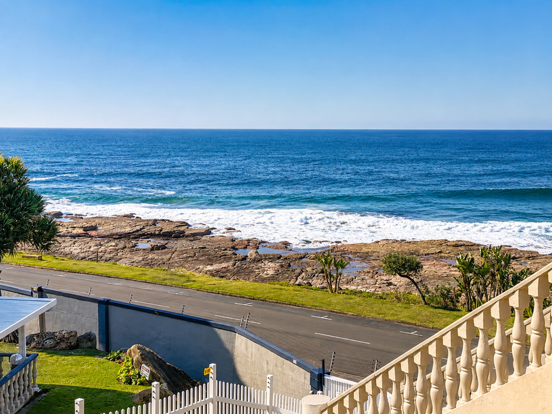 A scenic ocean view overlooking a coastal road, rocky shoreline, and surf, captured from an elevated balcony with a classic balustrade.